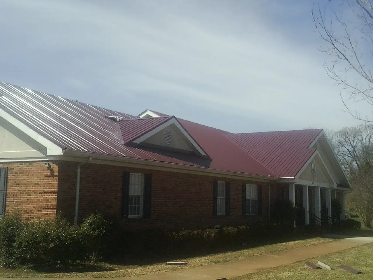 Red metal roof with gabled entries on a long brick building, from a Hail Damage Roof Repair job in Anchorage