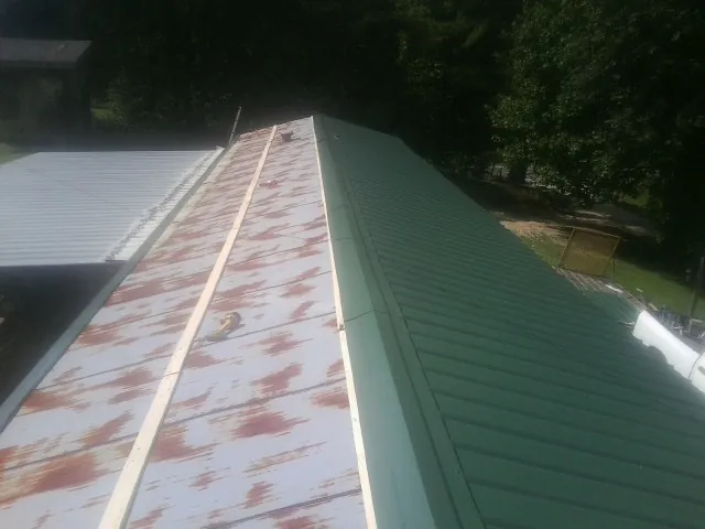 Old rusted panels beside newly installed green metal roofing — Wind Damage Roof Repair by Roofing Brothers in Anchorage
