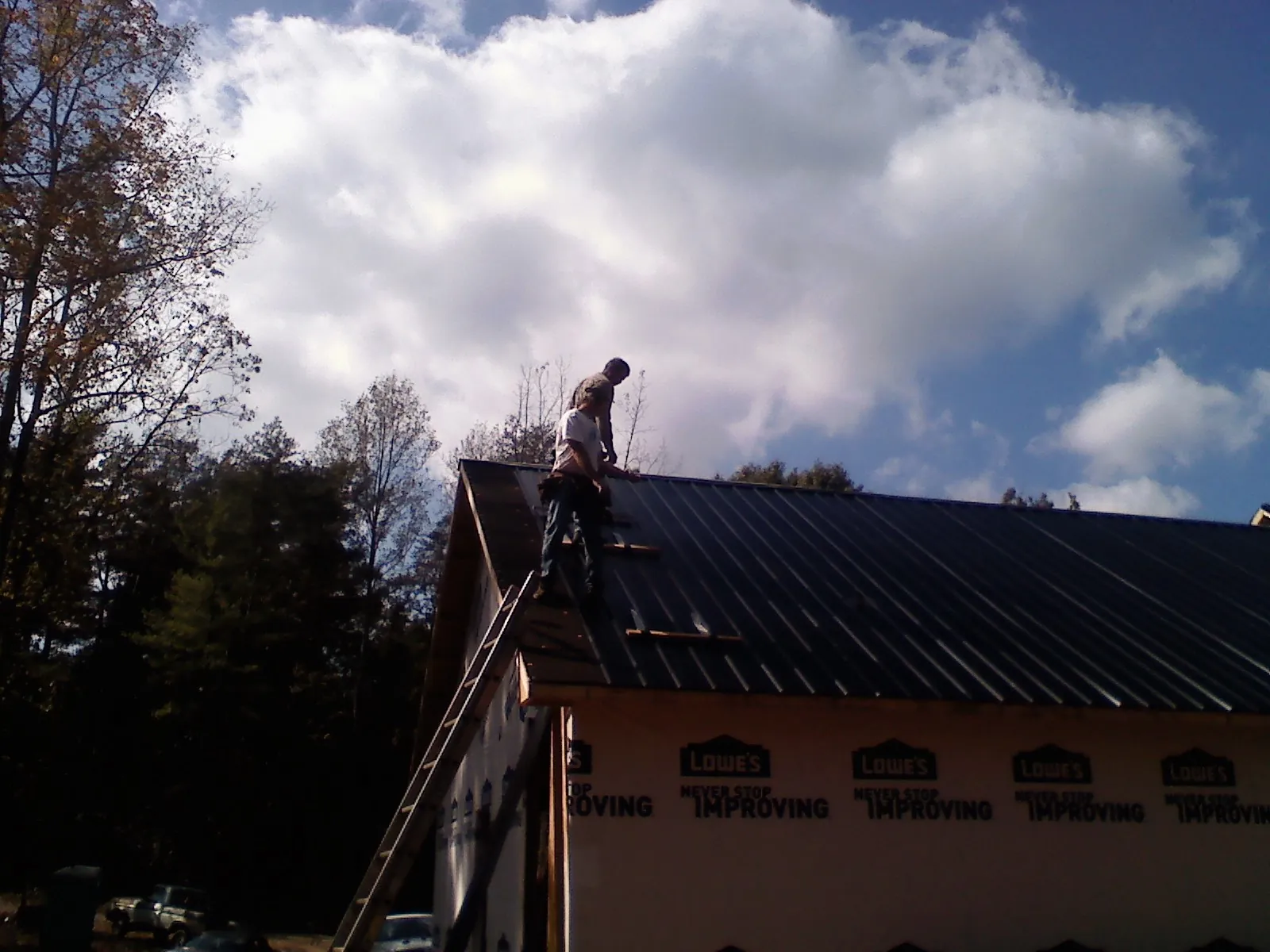 Roofer fastening dark metal panels high against a cloudy sky, from a Roof Inspection job in Anchorage