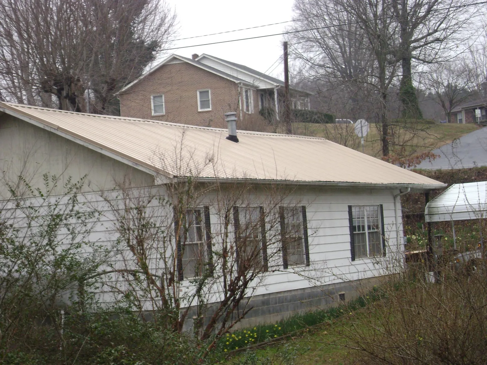 Tan metal roof on a white sided house set into a hillside — Commercial Roofing by Roofing Brothers in Anchorage